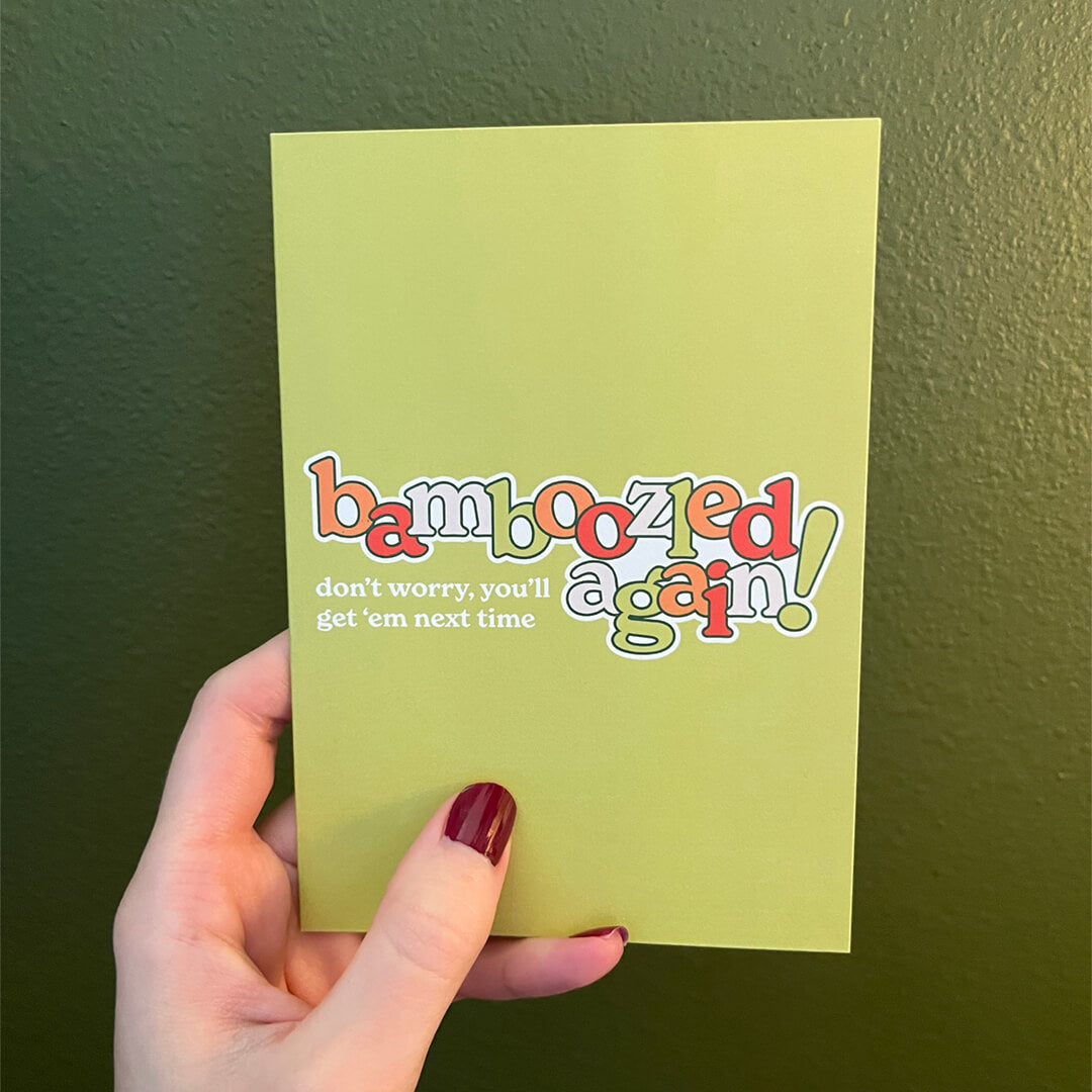 Hand holding a greeting card with the words, "Bamboozled Again! Don't worry, you'll get 'em next time."