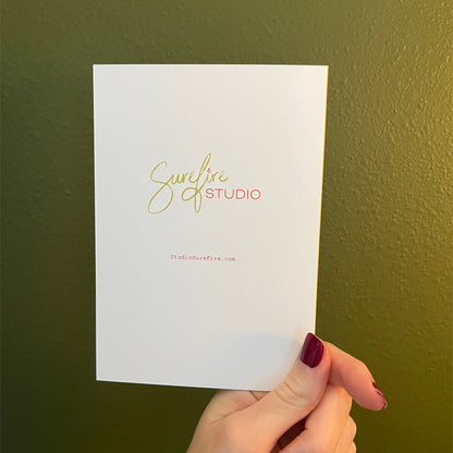 Hand holding a greeting card with the logo for Sure Fire Studio printed on it.