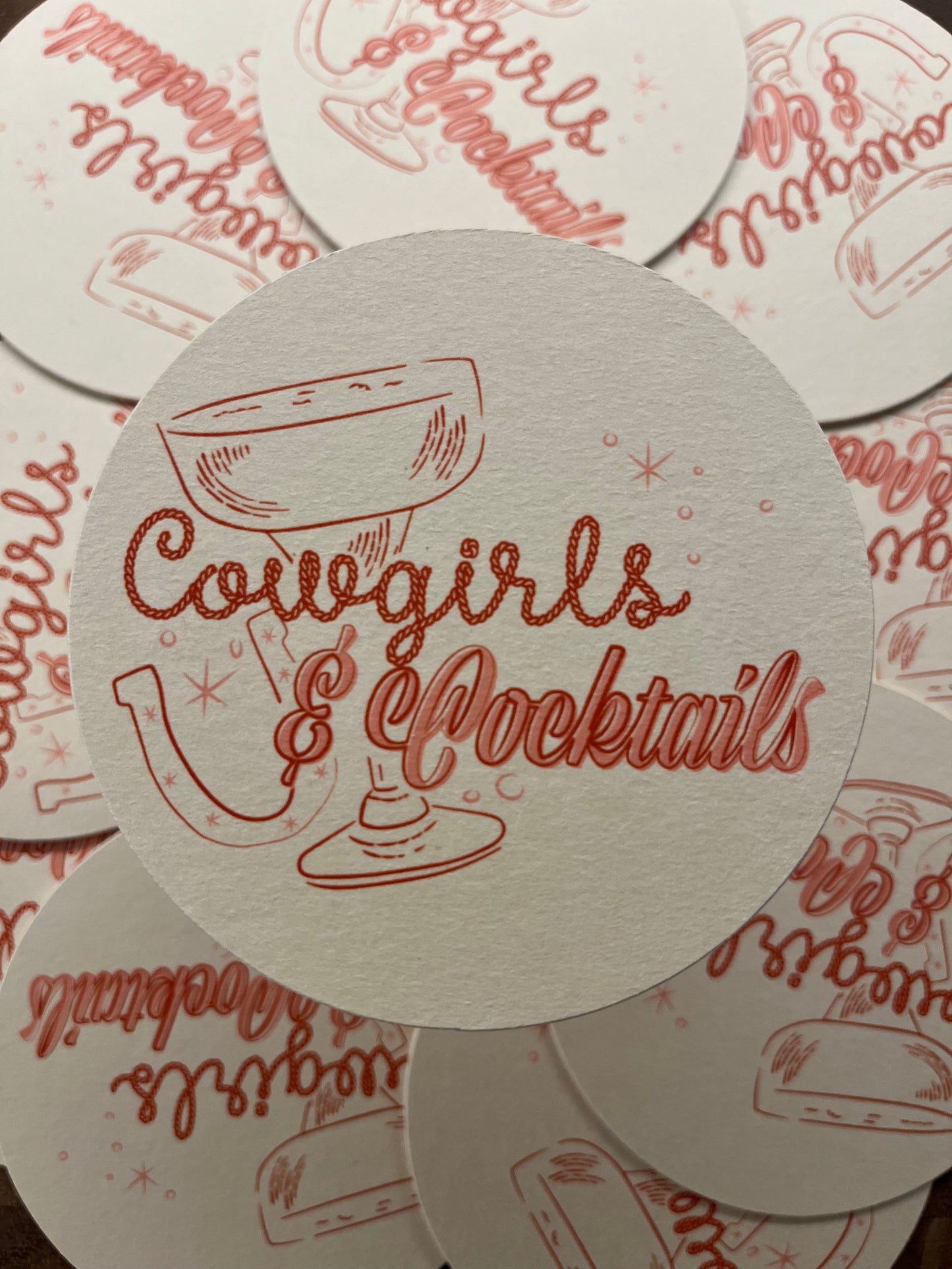 Pulpboard coaster that reads "Cowgirls & Cocktails" in a rope and script font with horseshoes and cocktails glasses.